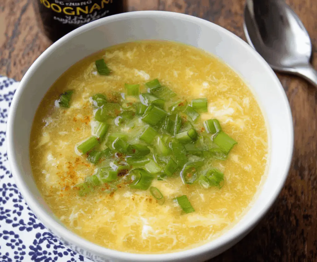 A bowl of hot, savory Egg Drop Soup garnished with chopped green onions and served in a white ceramic bowl.
