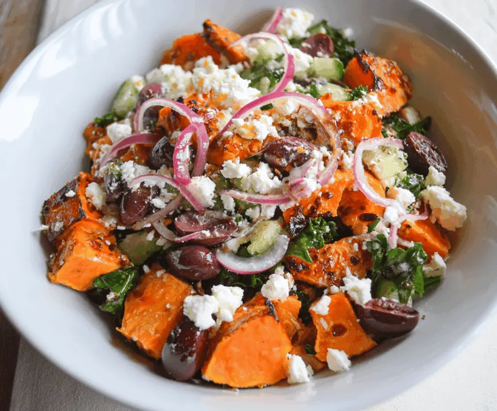 Colorful Sweet Potato Greek Salad with roasted sweet potatoes, cherry tomatoes, cucumbers, red onions, Kalamata olives, and crumbled feta cheese garnished with fresh herbs.
