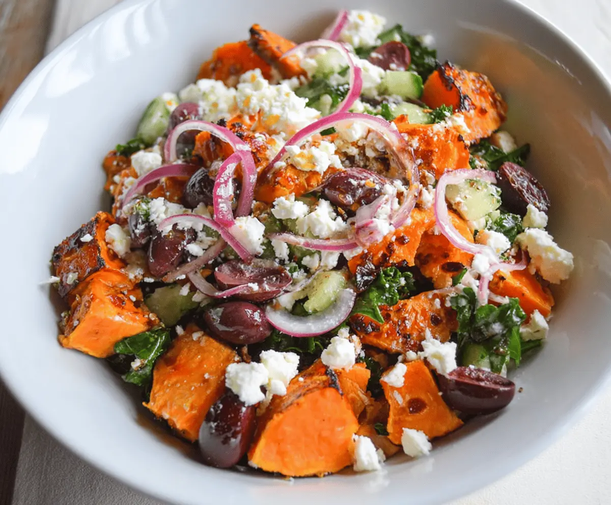 Colorful Sweet Potato Greek Salad with roasted sweet potatoes, cherry tomatoes, cucumbers, red onions, Kalamata olives, and crumbled feta cheese garnished with fresh herbs.