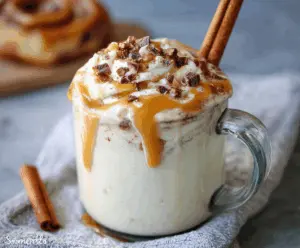 Delicious cinnamon bun white hot chocolate topped with whipped cream and cinnamon dust in a cozy mug.