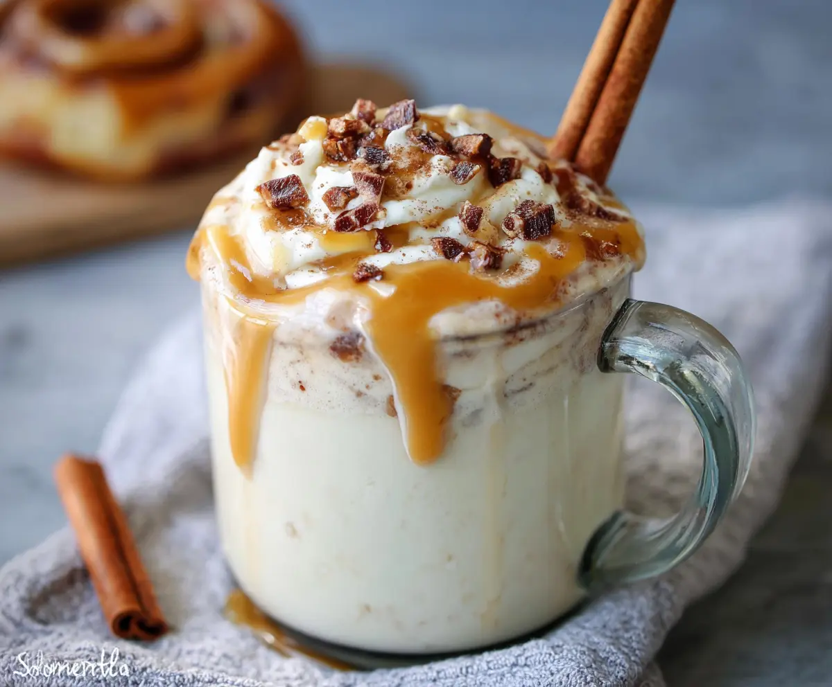 Delicious cinnamon bun white hot chocolate topped with whipped cream and cinnamon dust in a cozy mug.