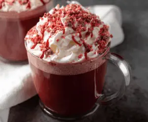 Creamy red velvet hot chocolate topped with whipped cream and red sprinkles in a cozy mug.