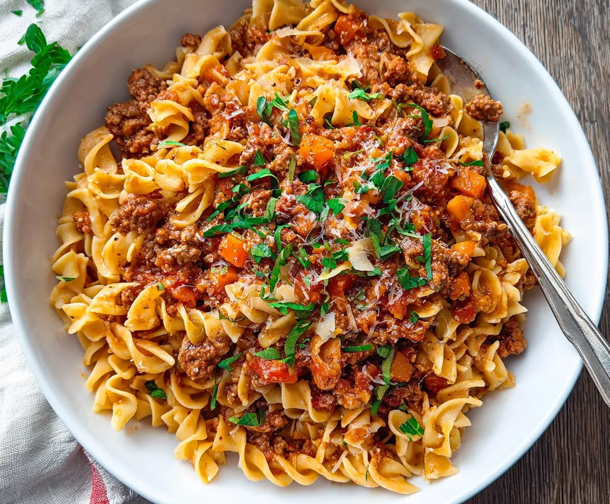 Delicious Pork Bolognese Pasta served on a white plate, garnished with fresh herbs.