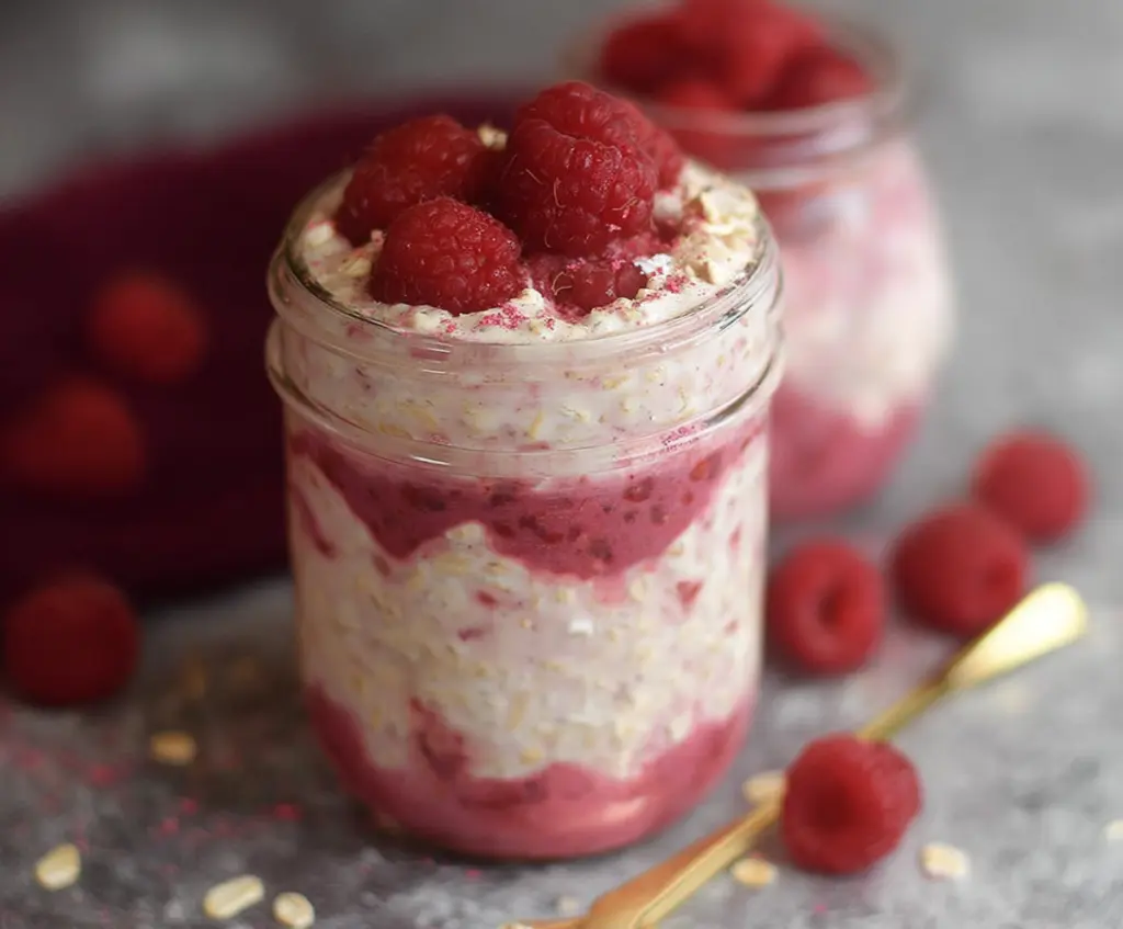 Creamy raspberry cheesecake overnight oats topped with fresh raspberries and a drizzle of honey.