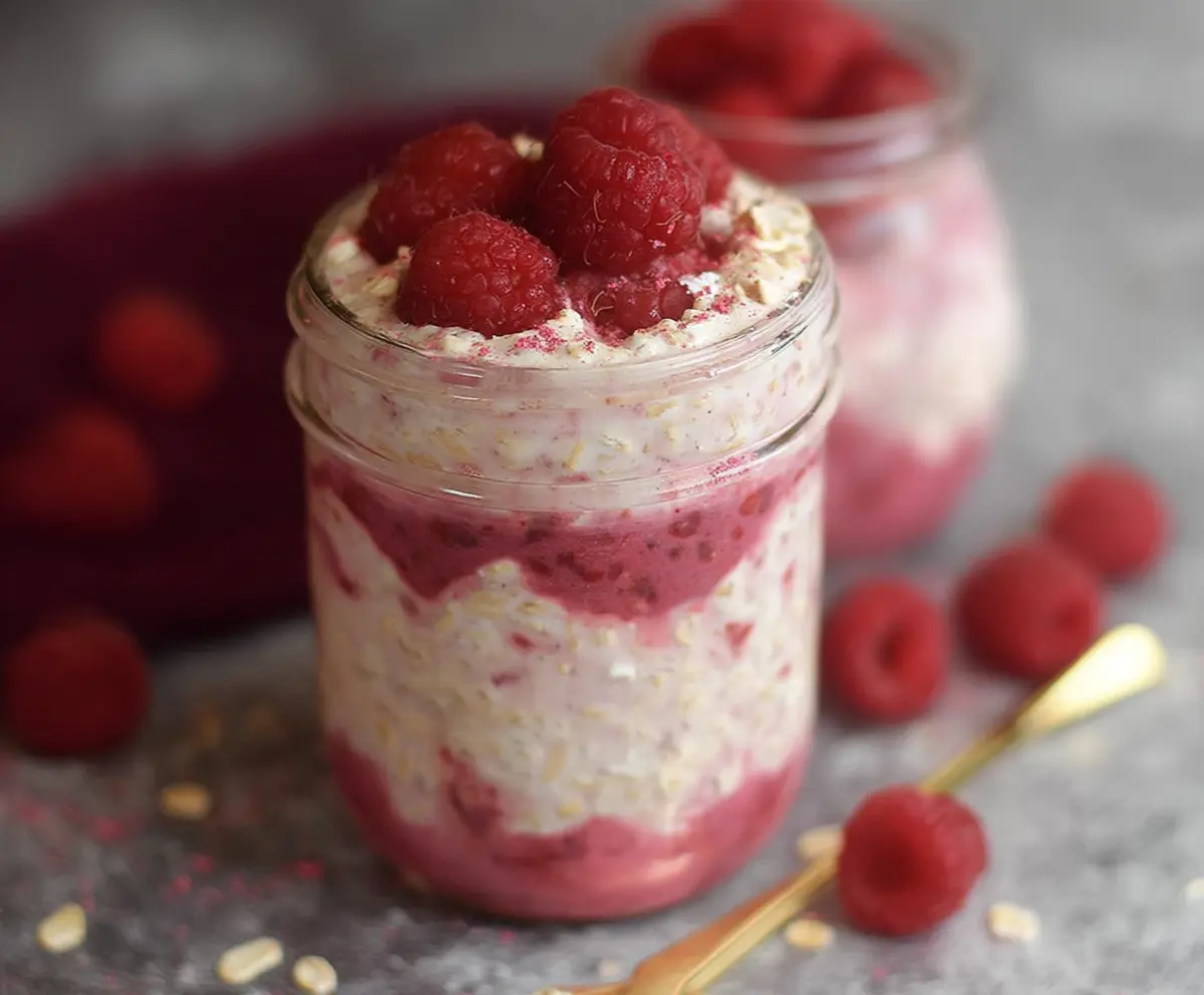 Creamy raspberry cheesecake overnight oats topped with fresh raspberries and a drizzle of honey.