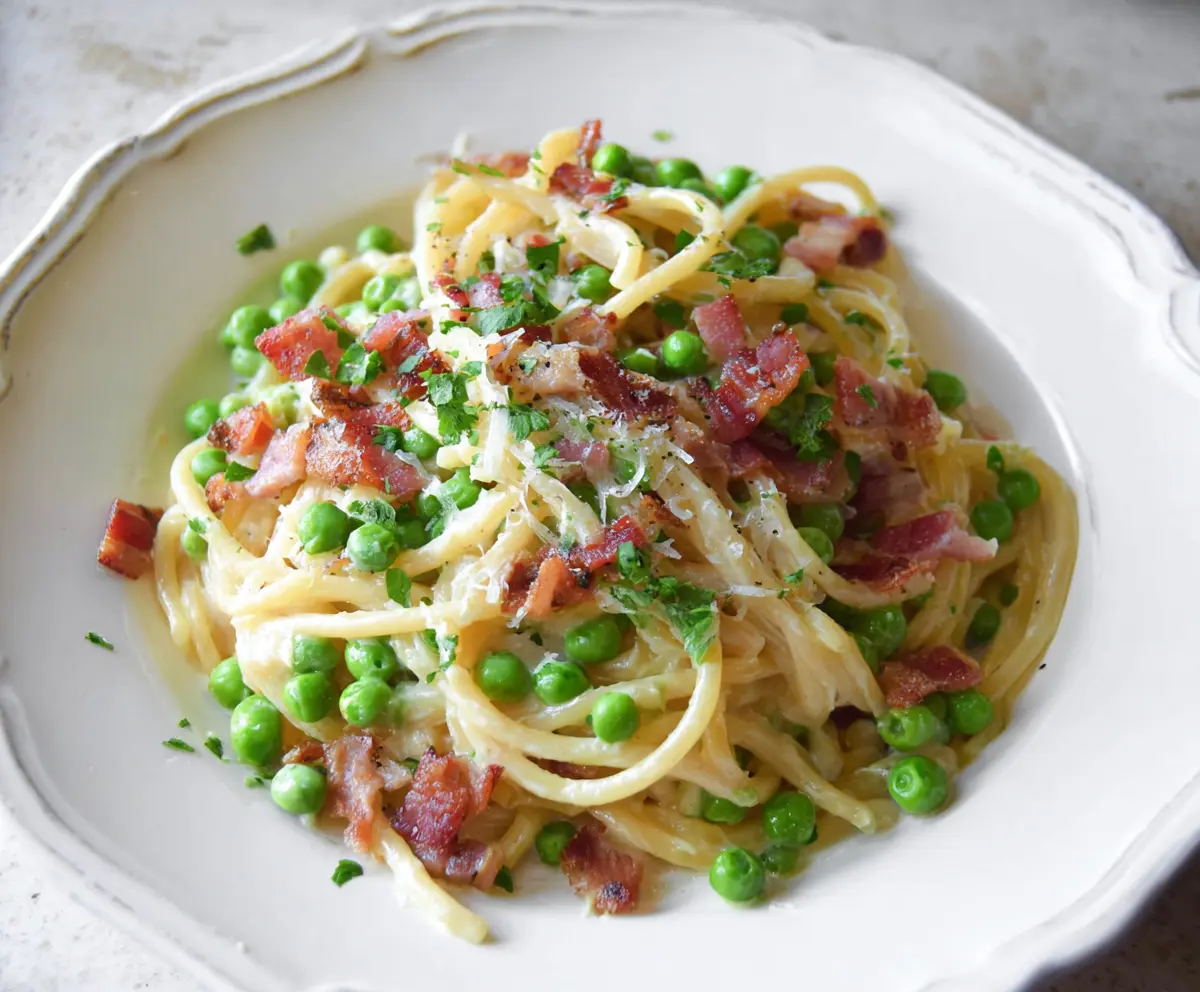 Delicious bacon and pea pasta dish served on a plate, garnished with fresh herbs.
