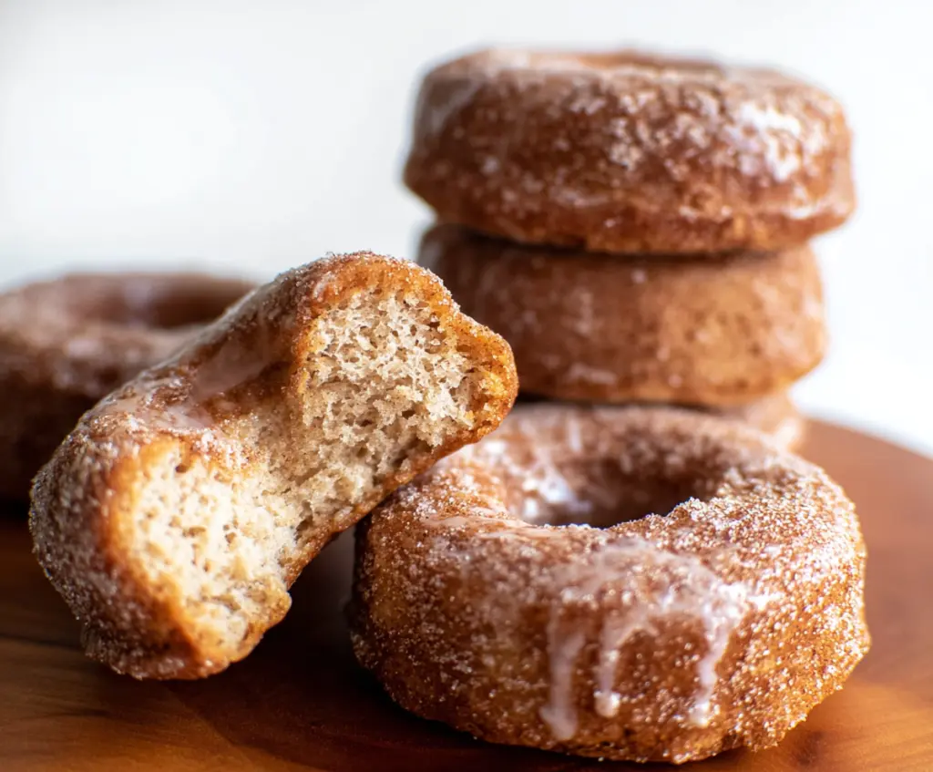 Homemade sourdough discard apple cider donuts bread on a rustic wooden table, showcasing a golden-brown crust and apple slices inside.