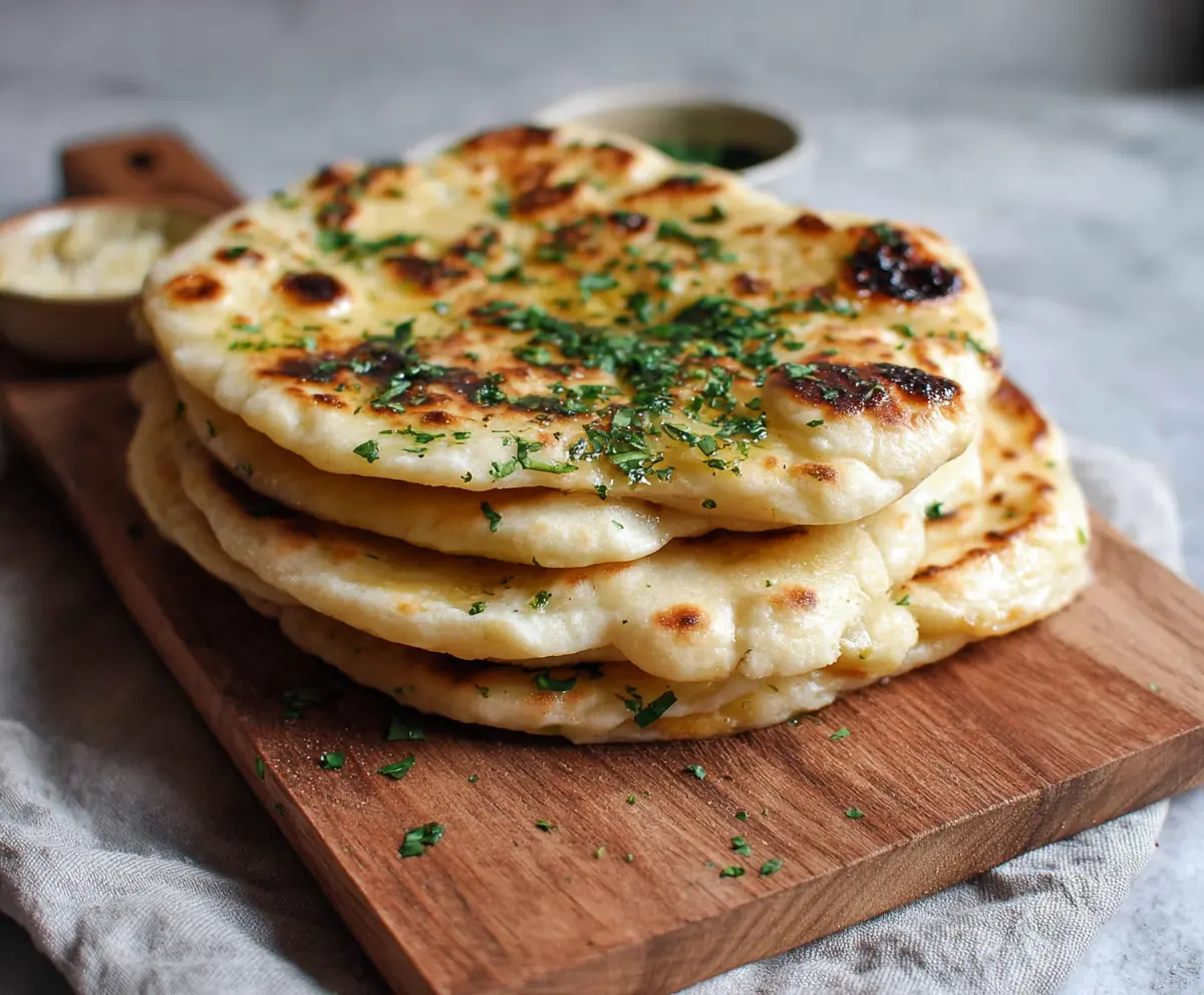 Homemade sourdough discard naan bread on a wooden serving platter, showcasing its soft and fluffy texture with a golden-brown crust.