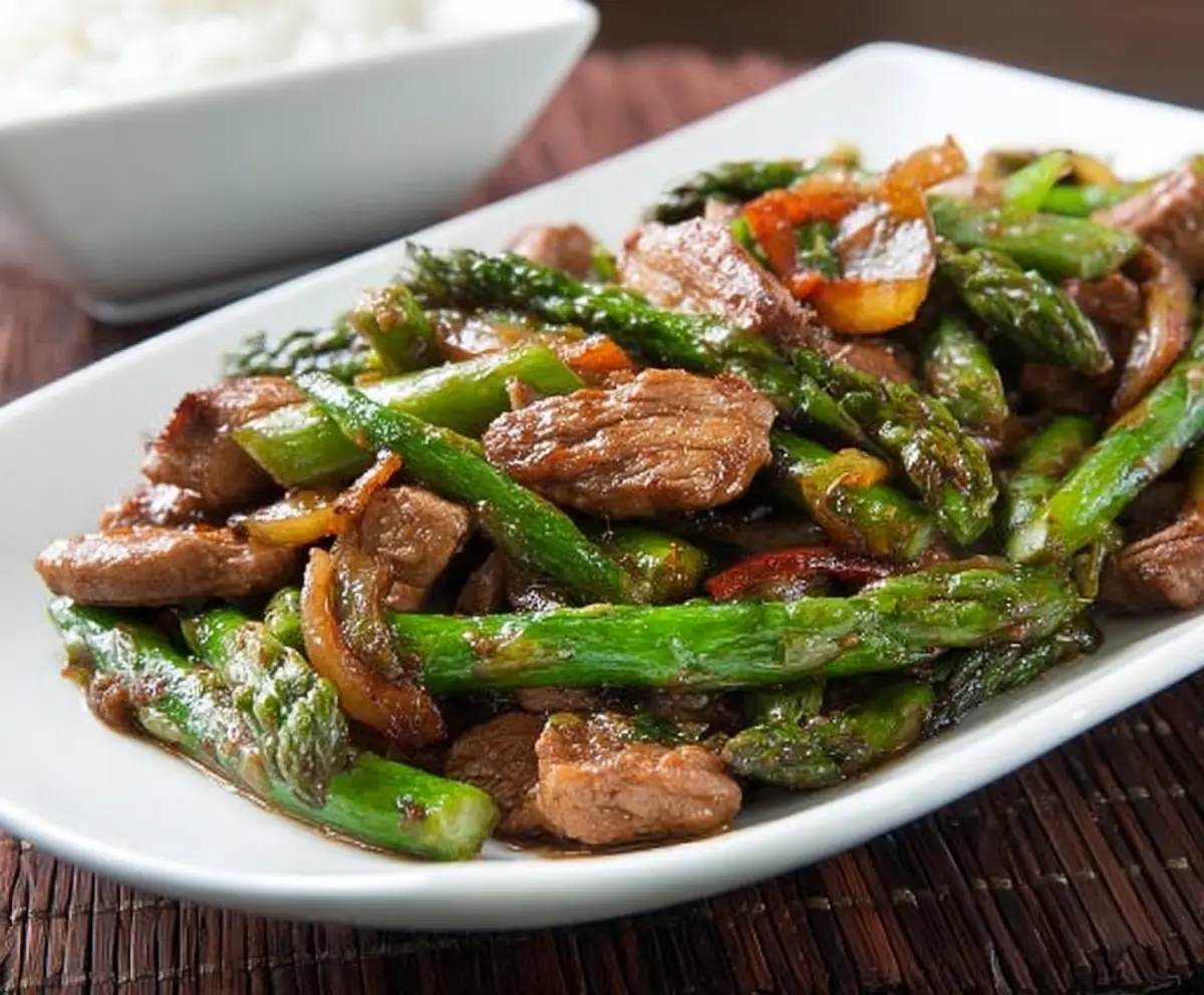 Delicious pork and fresh asparagus stir fry served in a white bowl.