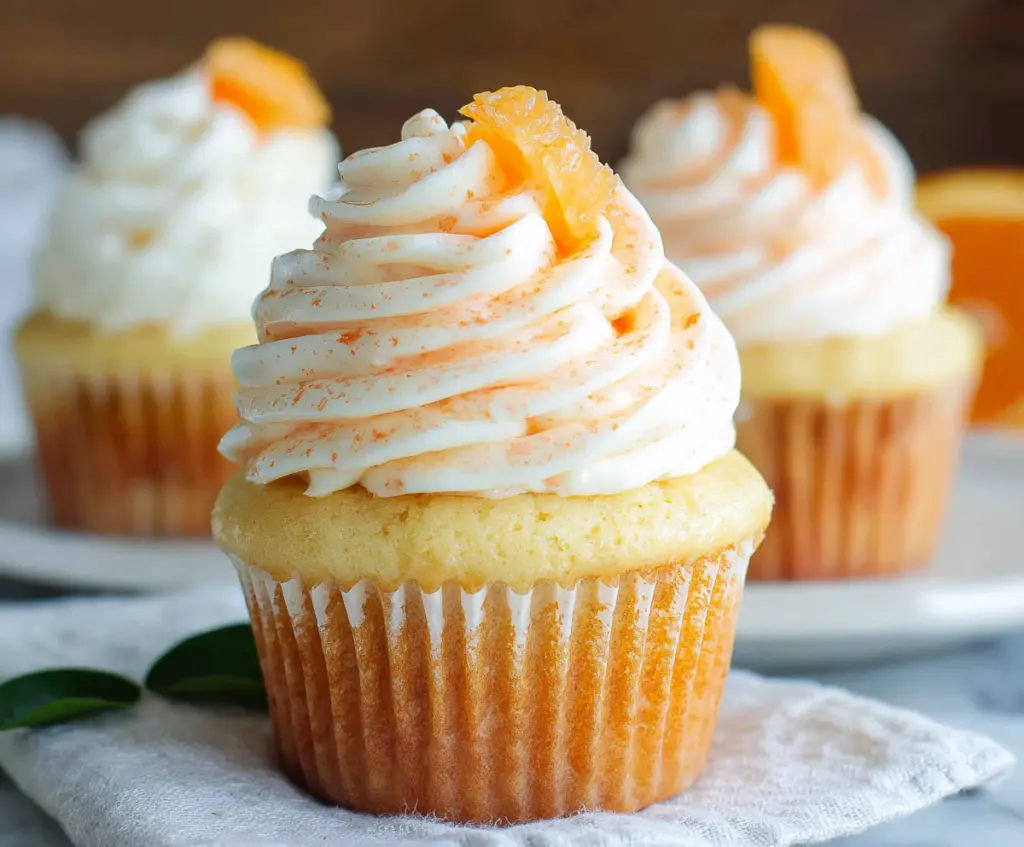 Delicious Orange Creamsicle Cupcakes with vibrant orange frosting and creamy filling on a plate.