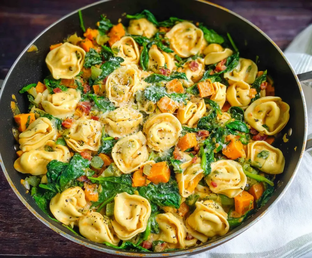 Delicious skillet tortellini with sweet potato and fresh spinach in a rustic pan.