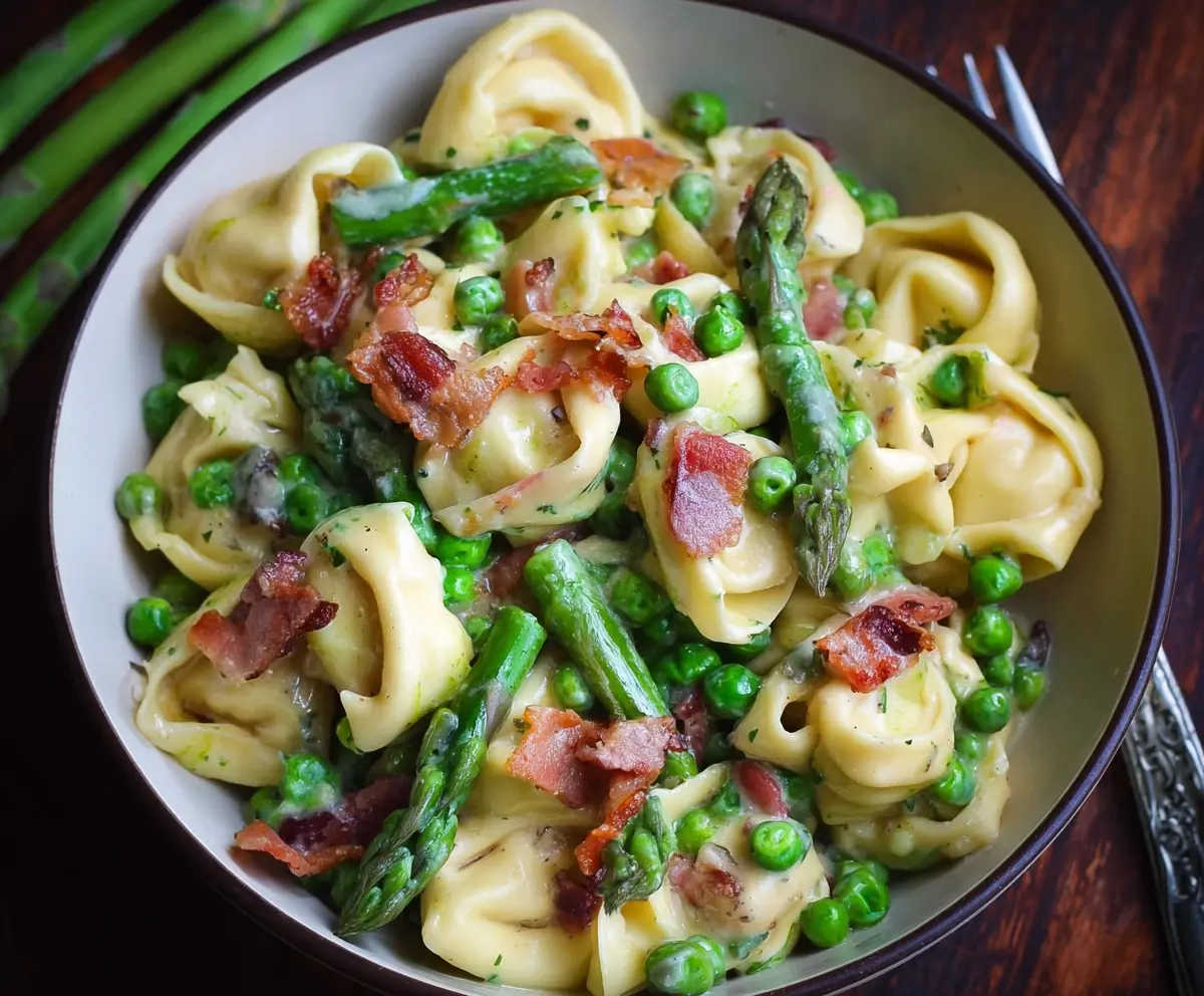 Delicious tortellini pasta with fresh peas, tender asparagus, and crispy bacon on a white plate.
